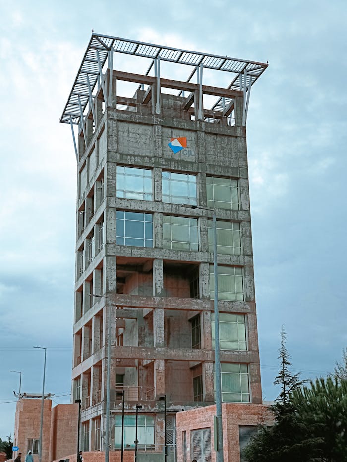 A tall, unfinished concrete tower under a cloudy sky in Madaba, showcasing modern architecture.